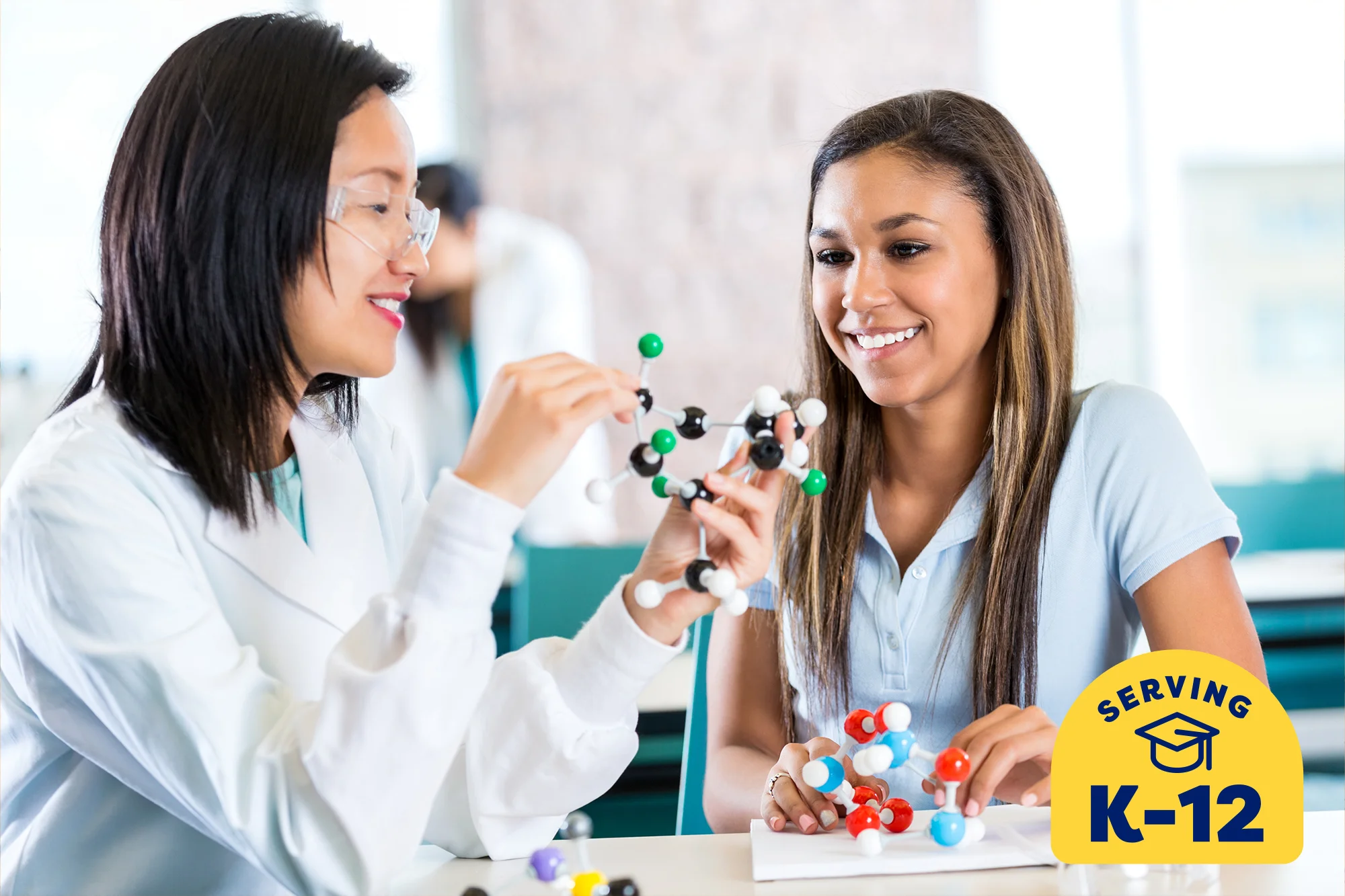 teacher wearing a lab coat and holding a molecular model and explaining it to her student